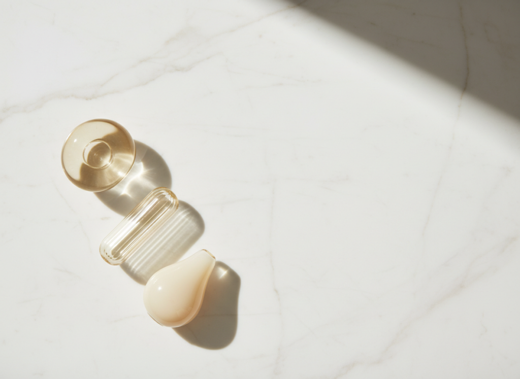 Unlabelled glass bottles arranged in a deliberate sequence on warm white marble — calm editorial flat lay