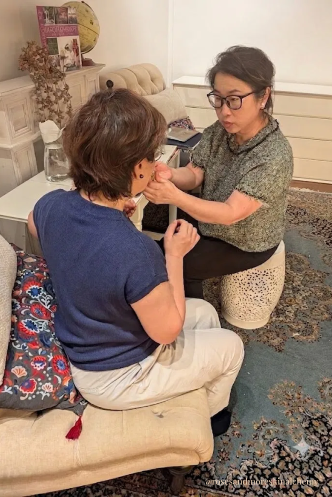 Jenny offers an unhurried skin consultation in Singapore, gently applying a botanical oil to a client's skin in a quiet corner of the loft at Roses & More Skin Alchemy.